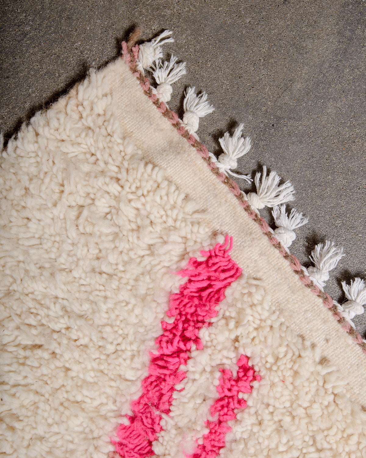 Corner of wool Azilal rug with short cotton tassels on cement floor.